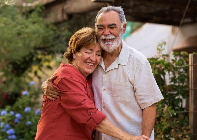 Older couple smiling and embracing outdoors.