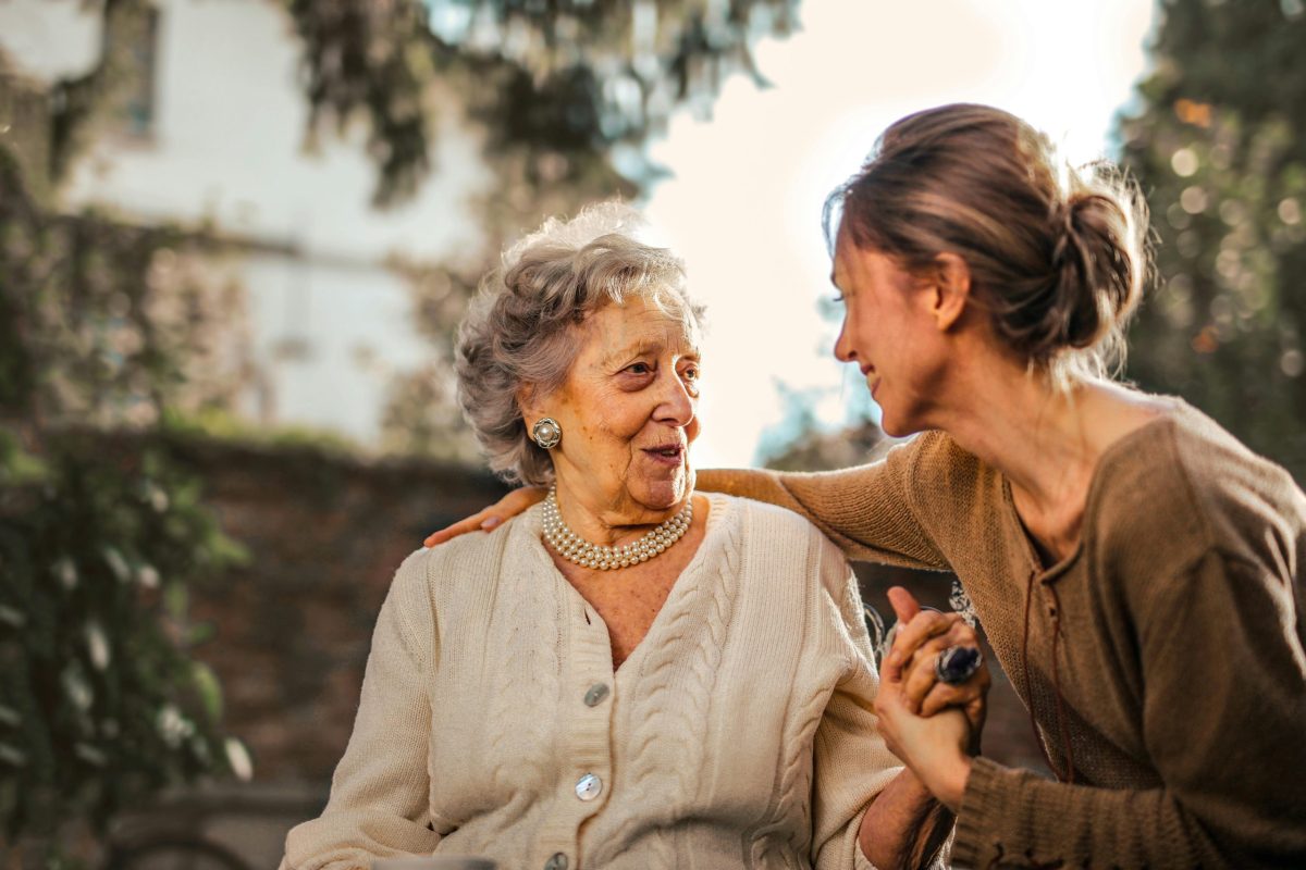 Older woman sitting on wheelchair conversing with a young lady.